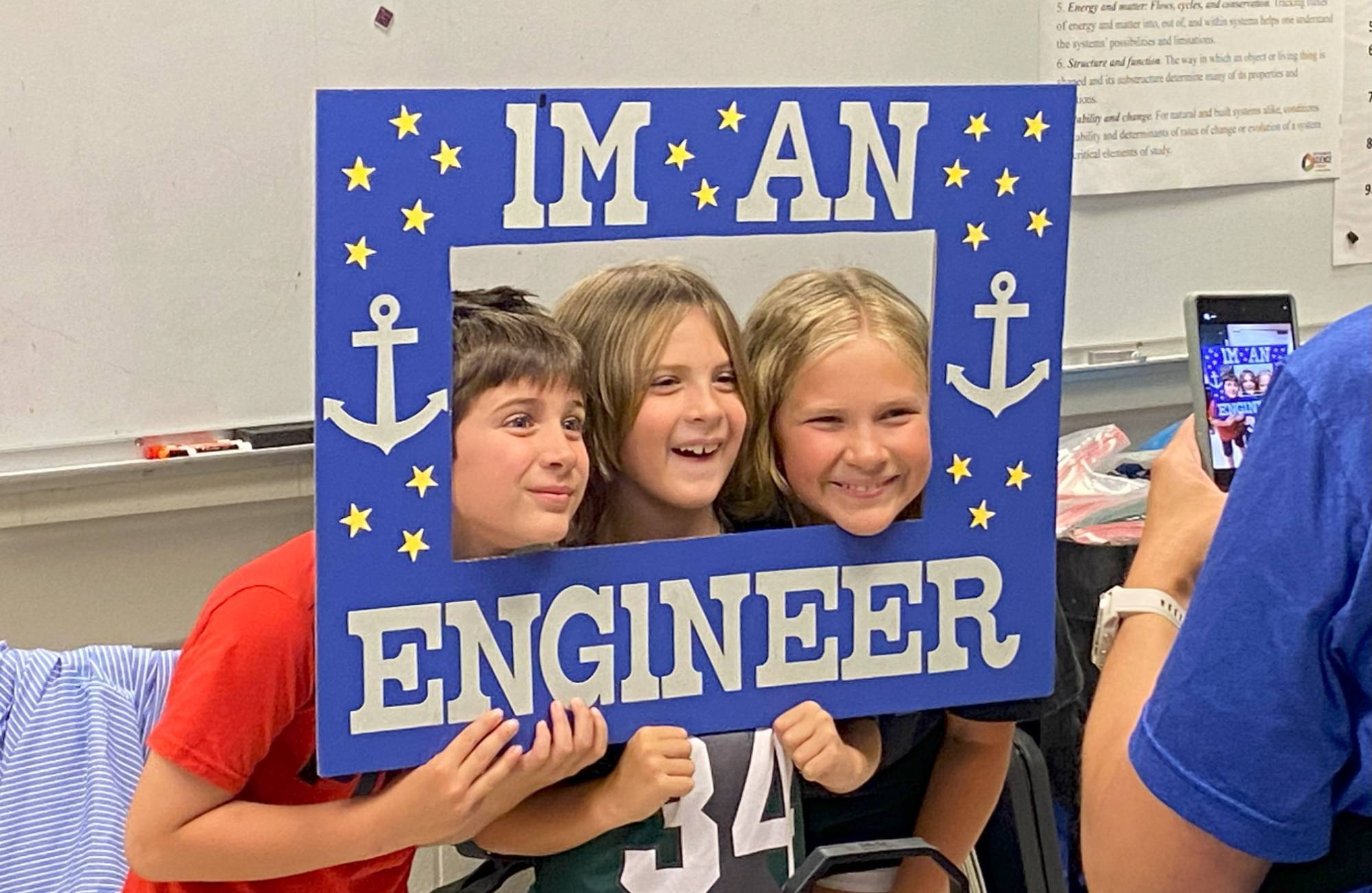 Three children pose in a poster board sign that says "I'm an Engineer"